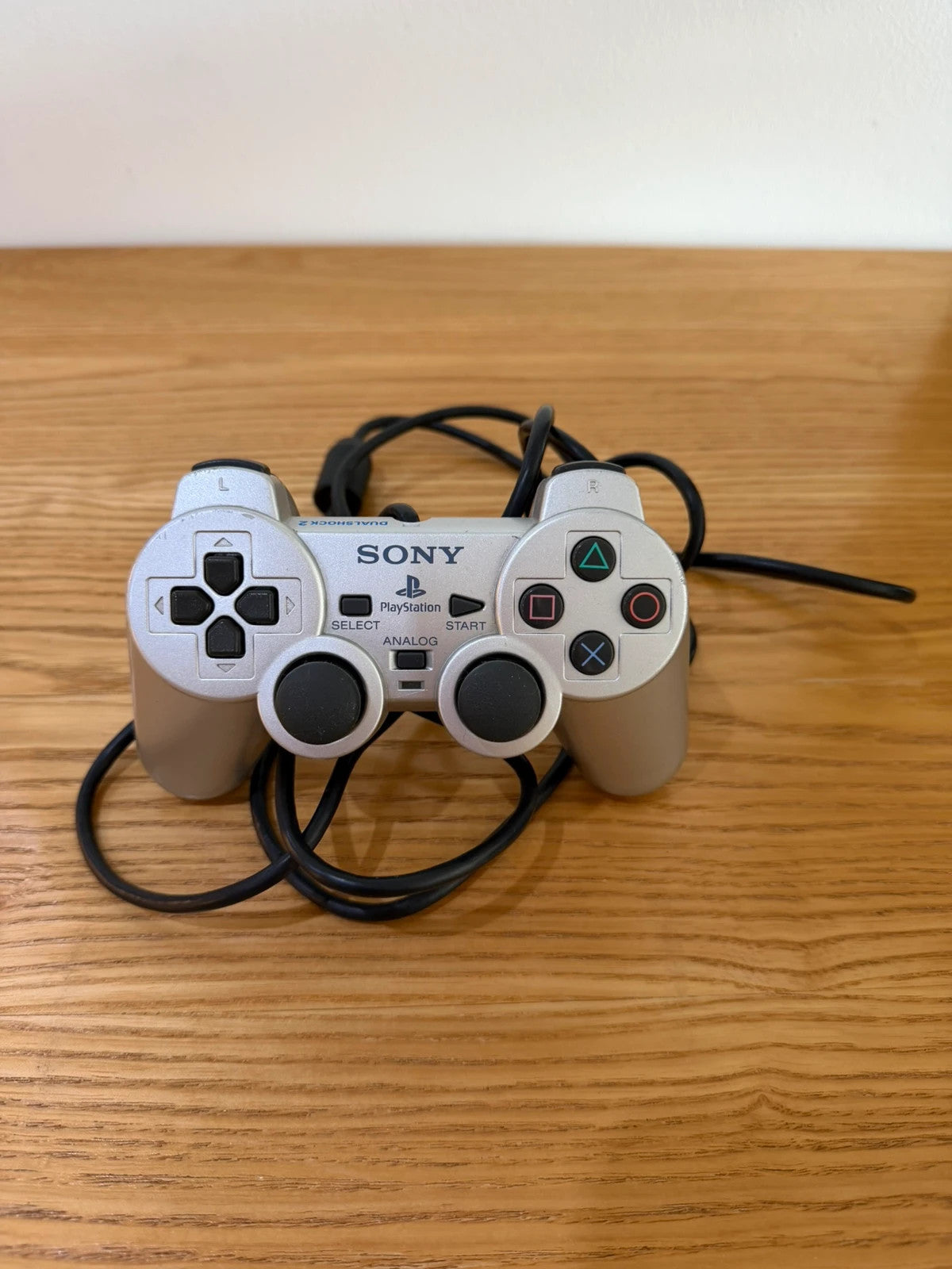 Sony silver PlayStation 2 controller with wired connection and minimal cosmetic wear.