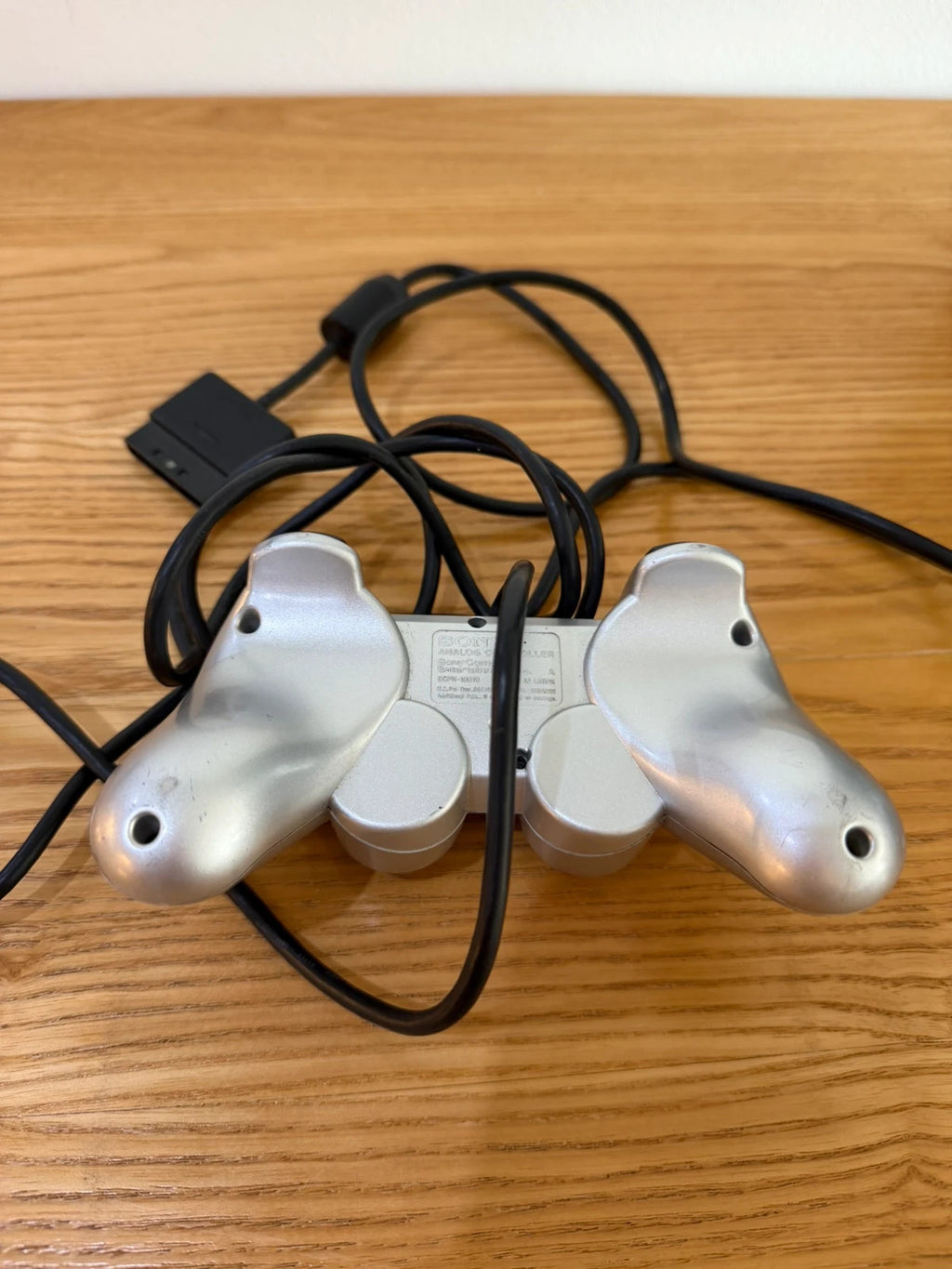 Sony silver PlayStation 2 controller with wired connection and minimal cosmetic wear.