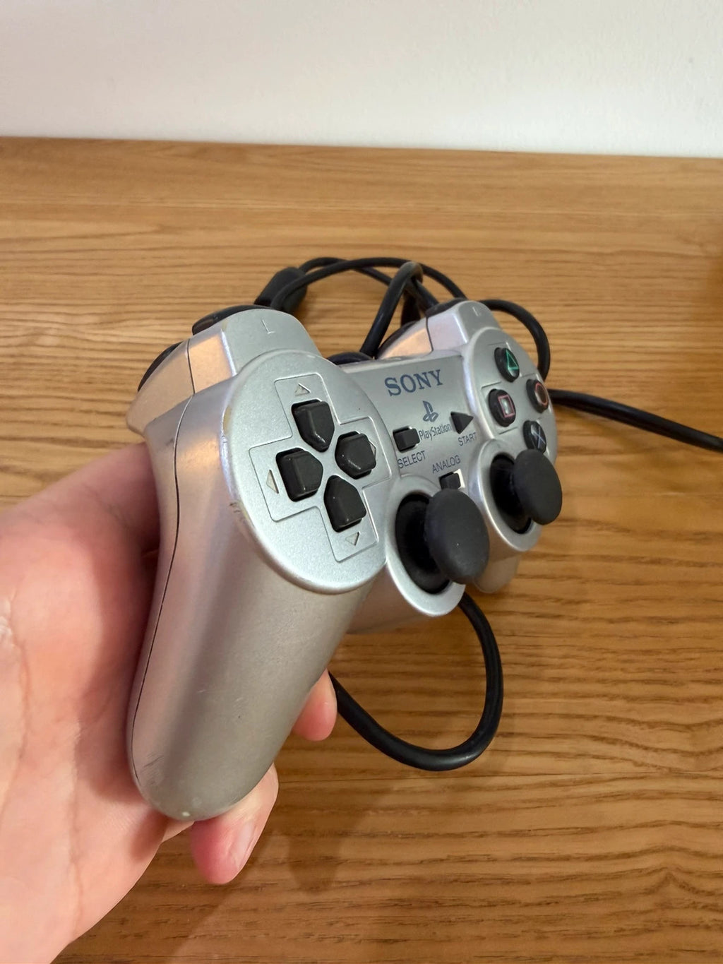 Sony silver PlayStation 2 controller with wired connection and minimal cosmetic wear.