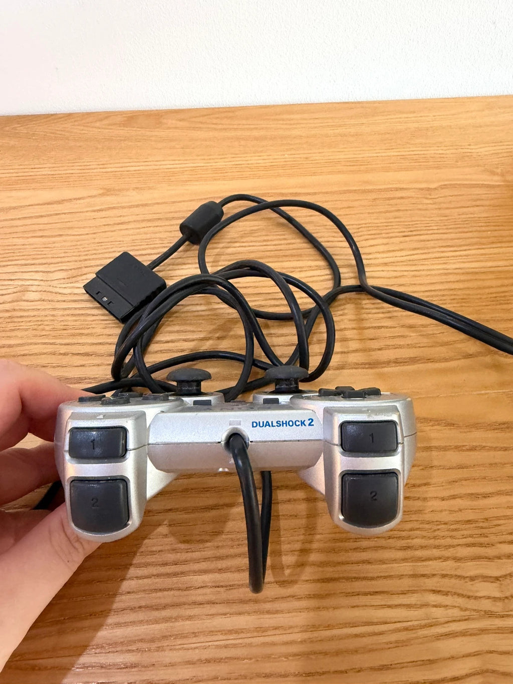 Sony silver PlayStation 2 controller with wired connection and minimal cosmetic wear.