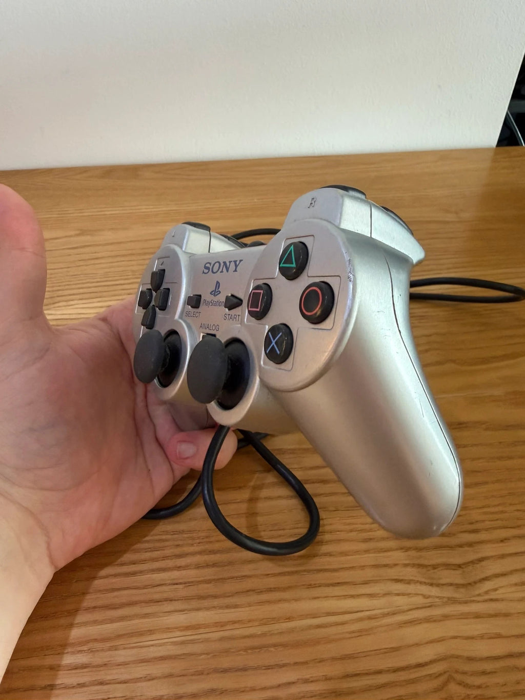 Sony silver PlayStation 2 controller with wired connection and minimal cosmetic wear.