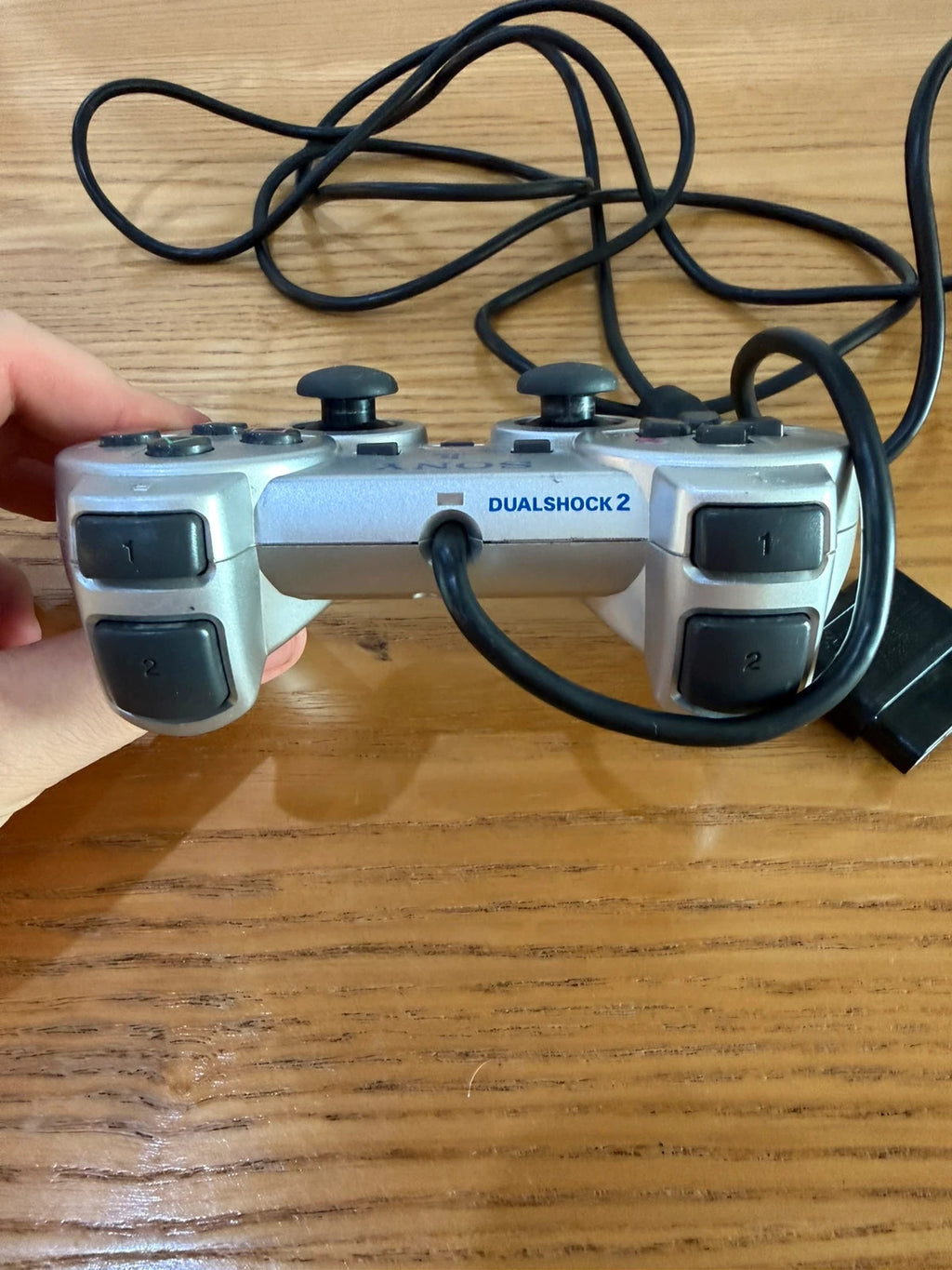Sony silver PlayStation 2 controller with wired connection and light signs of use.