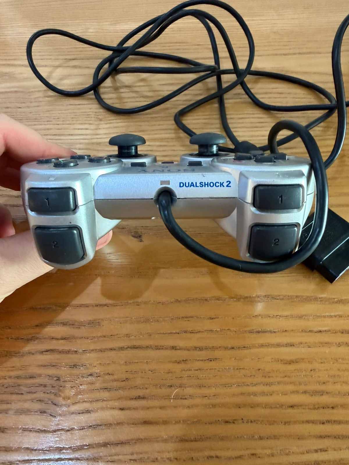 Sony silver PlayStation 2 controller with wired connection and light signs of use.