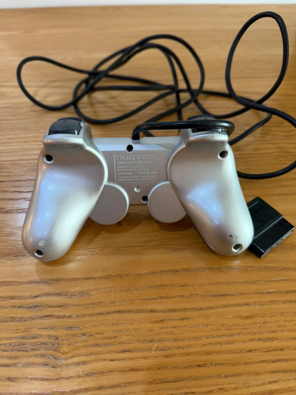 Sony silver PlayStation 2 controller with wired connection and light signs of use.