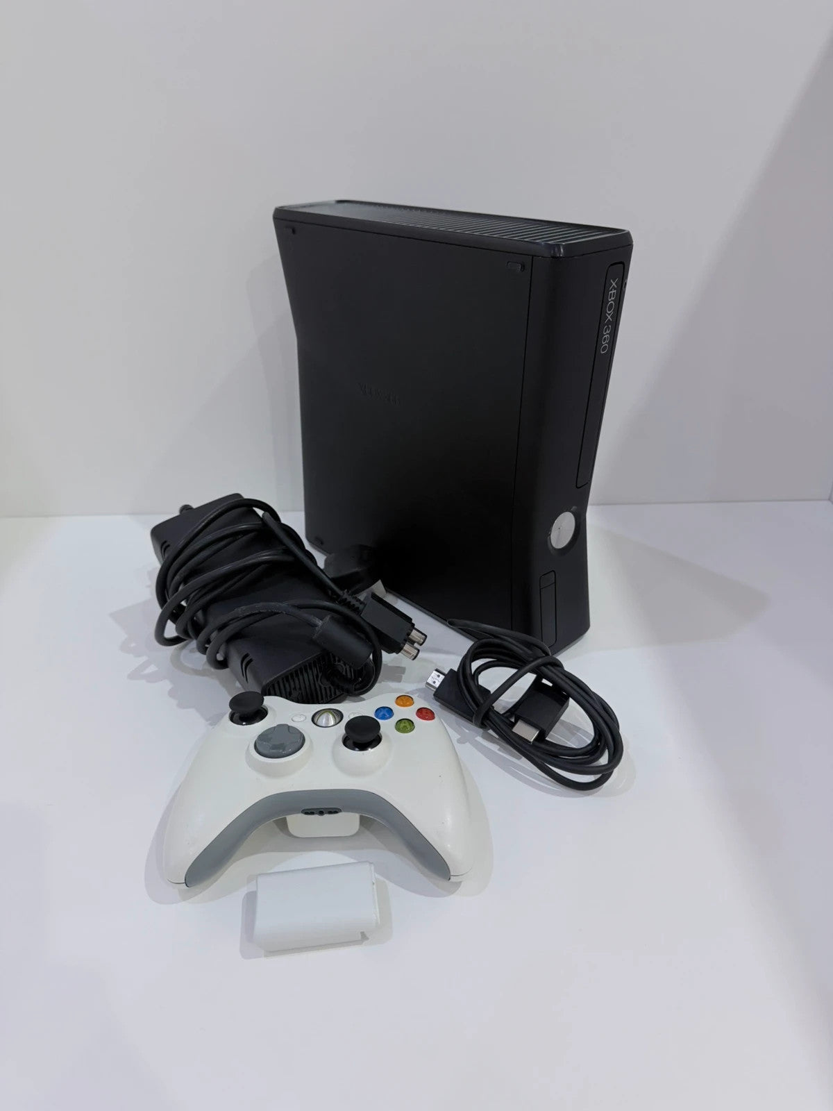 Xbox black video game console with white official controller and power supply cables.